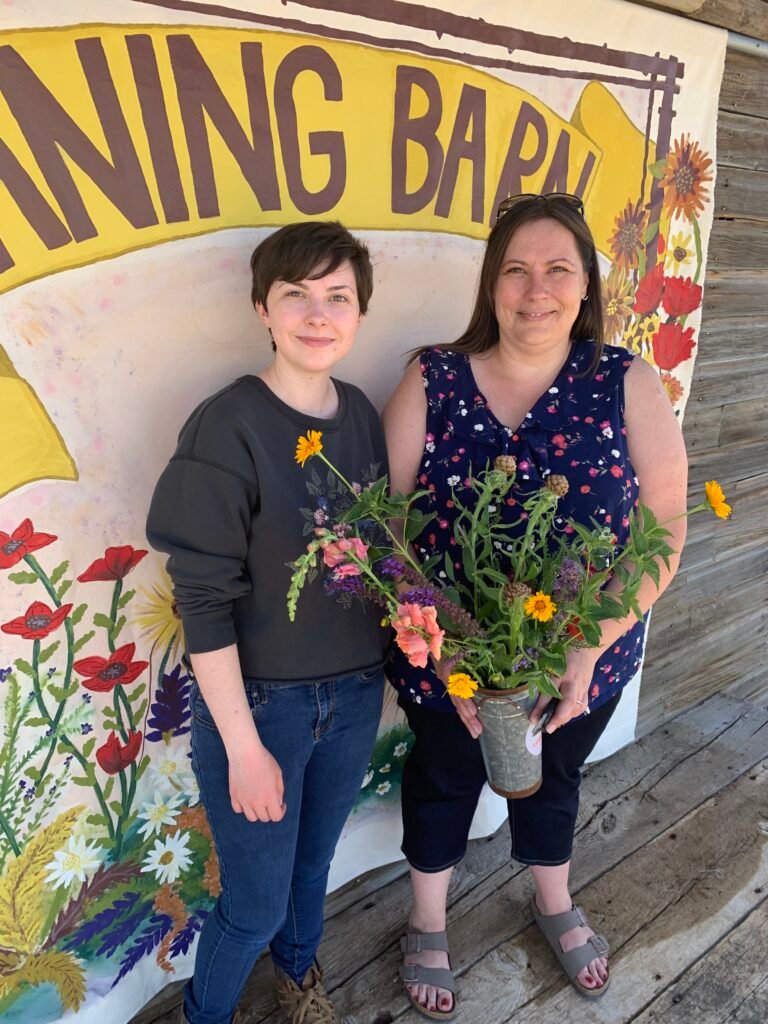 Brooklyn and their mother standing next together while their mother holds a pot of flowers. 