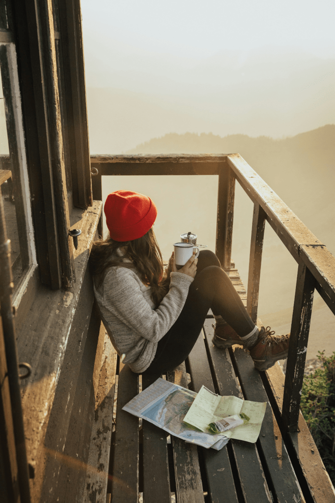 a woman sitting on her balcony dressed in warm clothing while drinking coffee and staring at the view