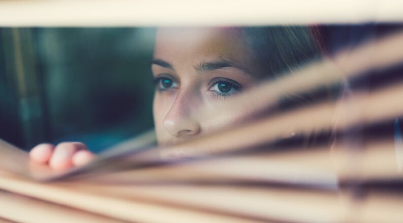 Woman peering through the venetian blinds