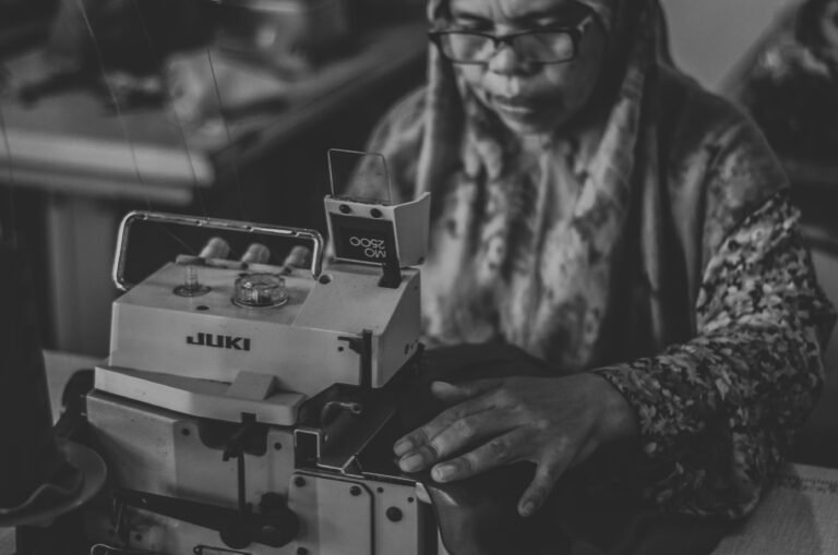 Black and white photo of an old exhausted woman using a sewing machine