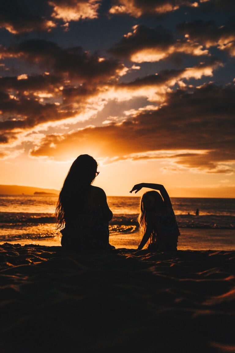 Silhouette of a mother and young daughter sitting on the beach with the sunset in the background