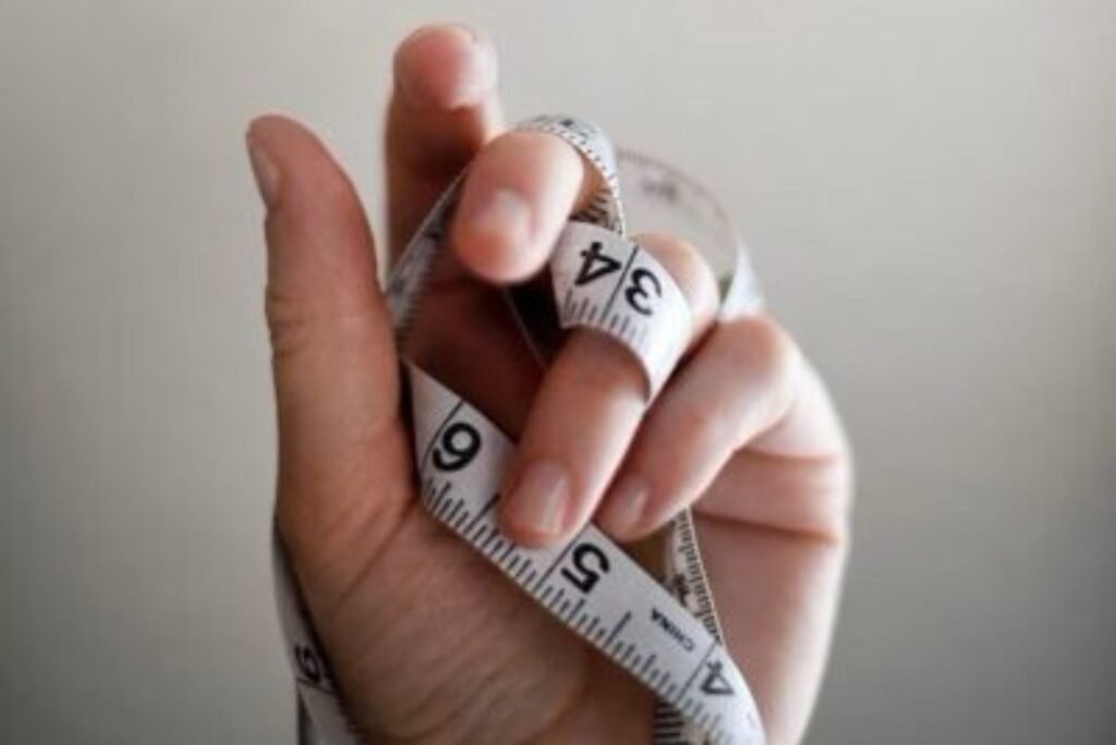 Single hand holding measuring tape, with the tape wrapped around the hand