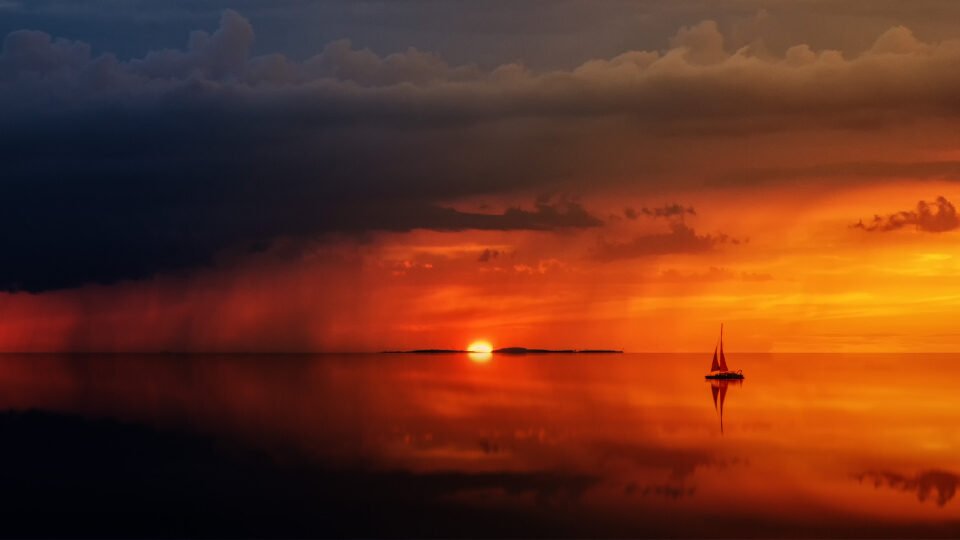 the sun setting in the ocean with a small ship in the water